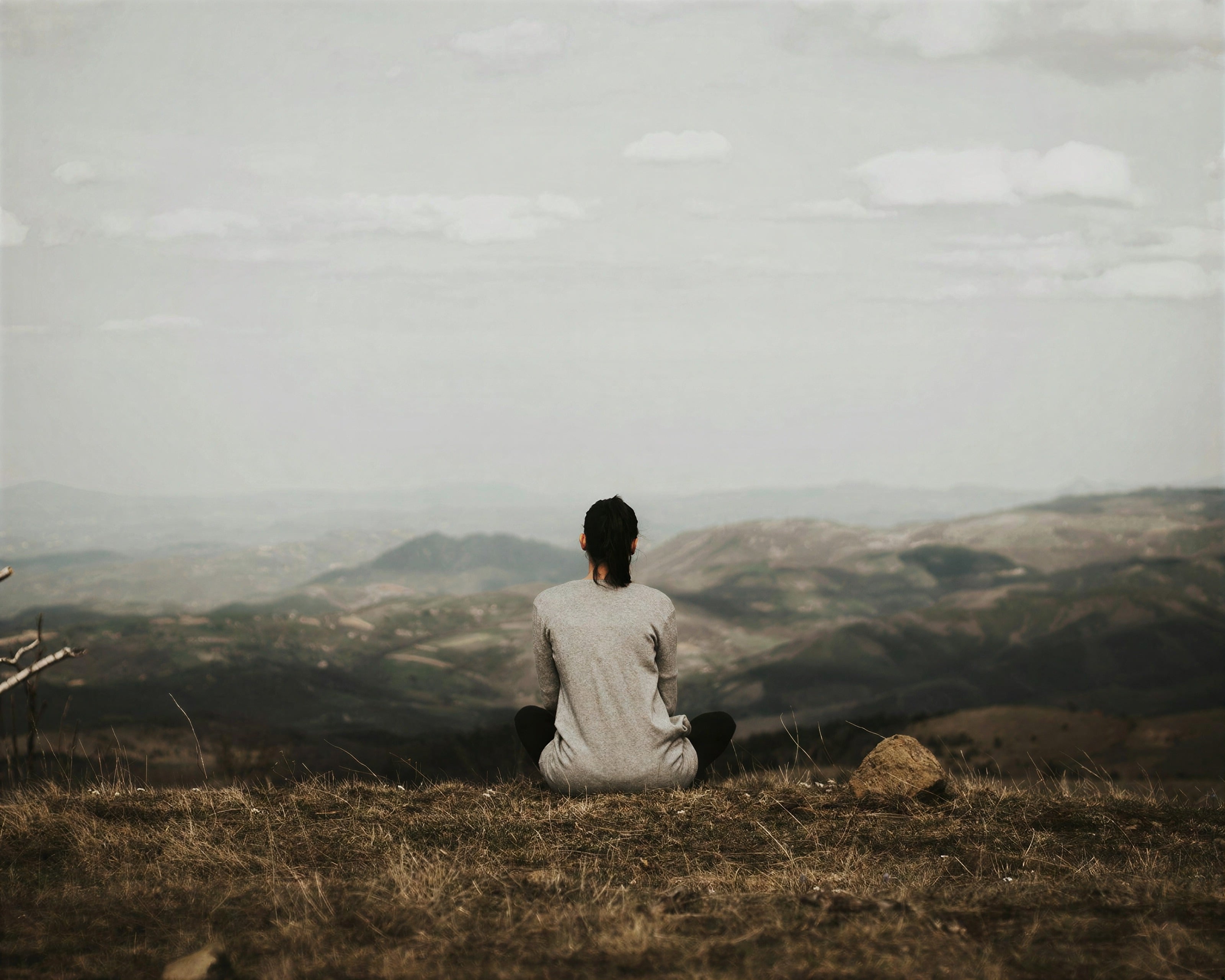 A woman sitting quietly on a hillside above a misty valley