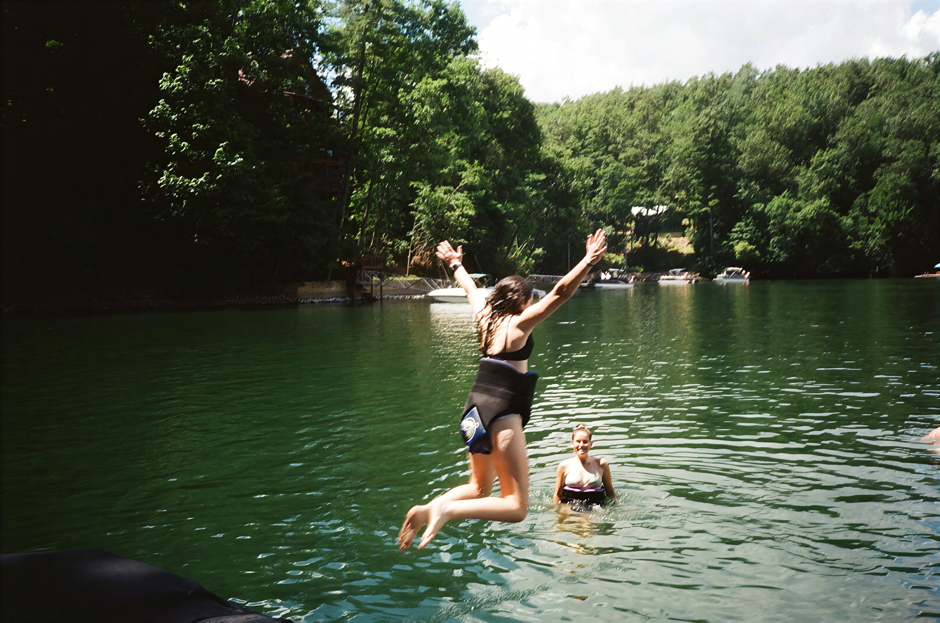 A guest leaping into a forest lake while a friend swims nearby