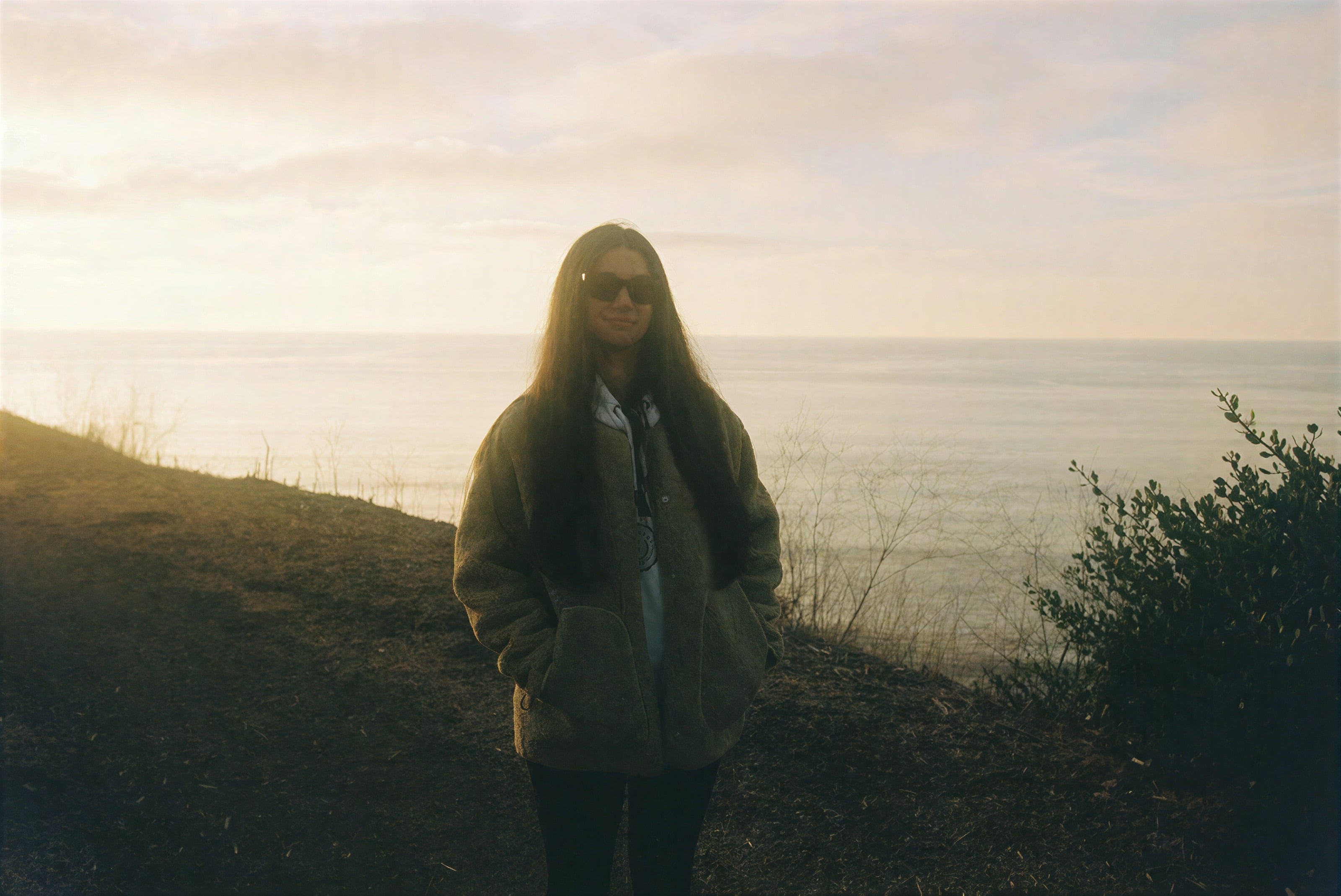 A woman standing on a clifftop above the sea at golden hour